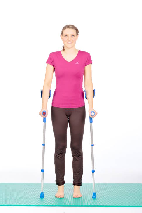 Ausgangsstellung: Das Gewicht ist auf beide Beine gleichmäßig verteilt. © Gelenk-Klinik Frau im Stand mit Krücken.