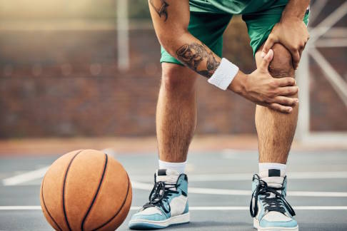 Im fortgeschrittenen Stadium des Patellaspitzensyndrom treten bei jeglicher Belastung des Kniegelenks starke Schmerzen auf. Sport ist dann nicht mehr möglich. © Clement Coetzee/peopleimages.com, Adobe Basketballer mit Knieschmerzen vorne