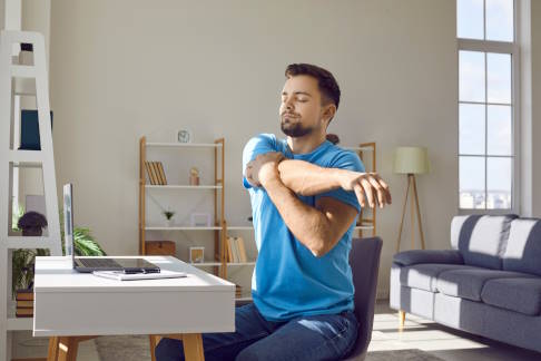 Regelmäßige Dehnübungen, auch am Arbeitsplatz, halten die Sehnen geschmeidig und beugen Tendinopathien vor. © Studio Romantic, Adobe Mann am Schreibtisch dehnt sich