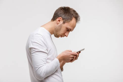 Vor allem unsere heutige moderne Lebensweise begünstigt die Entstehung eines Rundrückens. © DimaBerlin, Adobe Mann starrt mit nach vorne geneigtem Kopf auf sein Smartphone.